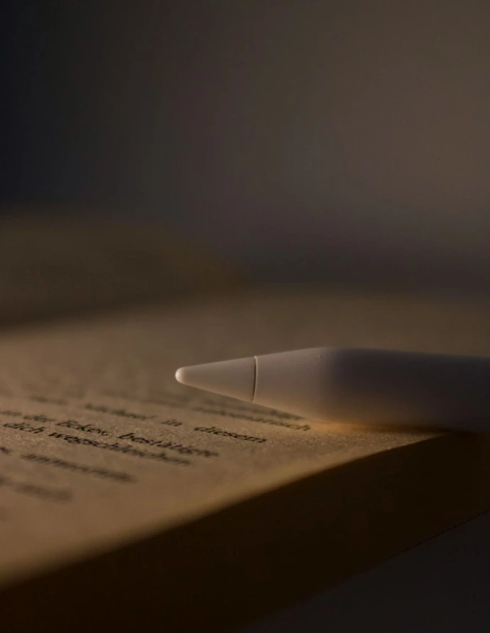 A white stylus rests on an open book.